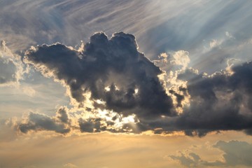 evocative image of the sun hiding behind a large dark cloud at sunset