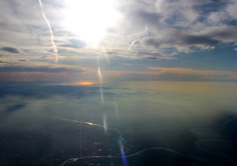 Naklejka na ściany i meble spectacular sunset seen from an airplane with the sun reflecting off a river and the mountains in the background