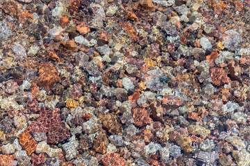 Sun glare on transparent water through which multi-colored stones are visible. Eilat Gulf of the Red Sea