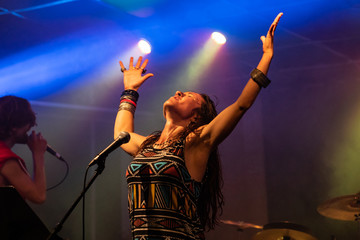 a female musician is viewed from a low angle as she sings and performs with hands raised, blurry...