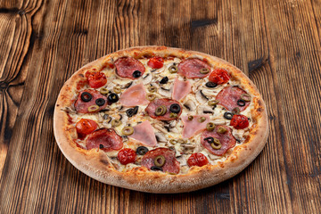 Hot meat pizza with pepperoni, salami, ham, melted cheese and olives on wooden table