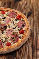 Hot meat pizza with pepperoni, salami, ham, melted cheese and olives on wooden table