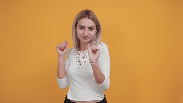 Young beautiful blonde woman wearing white shirt over isolated orange background smiling and laughing, dancing doing rock symbol with hands up. Music star. Funny concept.