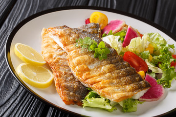Tasty recipe for spicy grilled sea bass fillet with lemon and vegetable salad close-up on a plate....