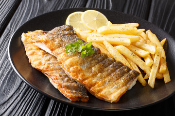 Menu of fried sea bass fillet with lemon and french fries close-up on a plate. horizontal
