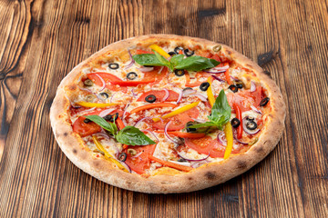 Vegetable pizza with melted cheese, bell pepper, tomatoes and olives on wooden table