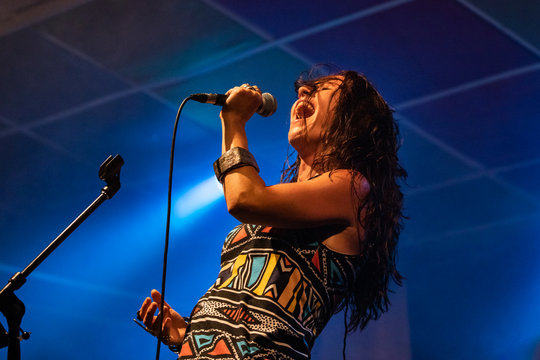 A female musician is viewed from a low angle as she sings, with open mouth in microphone during a performance on stage
