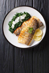 Grilled sea bass fillet with spinach garnish in a creamy sauce closeup on a plate. Vertical top view