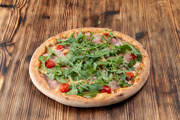 Parma ham pizza with fresh arugula and cherry tomatoes on wooden table