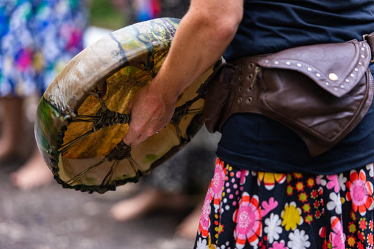 close up on caucasian woman's hand holding her sacred drum, new colourful native american leather drum while playing outside with some friends