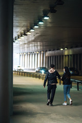 Back view of young couple  holding hand going through a dark tunnel. Stylish couple in love hug each other on the black background with lights. Together. Love, romantic, tenderness concept.