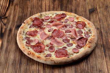 Italian meat pizza with sausages, pepperoni, spicy chorizo and melted cheese on wooden table