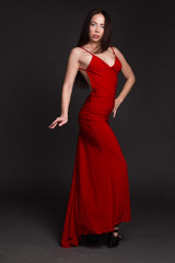 portrait of a young dark-haired girl on a dark background, dancing in a red long dress