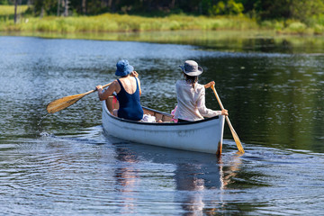 selective focus on mother and daughter are seen from the back as they riding small wooden boat and Rowing on the lake, with blurred trees on the background