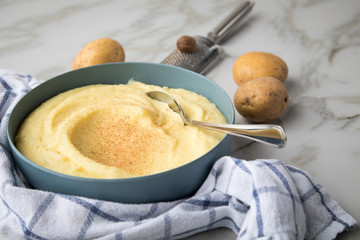 Schale Schüssel mit Kartoffelpüree mit Zutaten aus Kartoffeln, Muskatnuss dazu Küchentuch und Muskatreibe auf hell Marmor Hintergrund