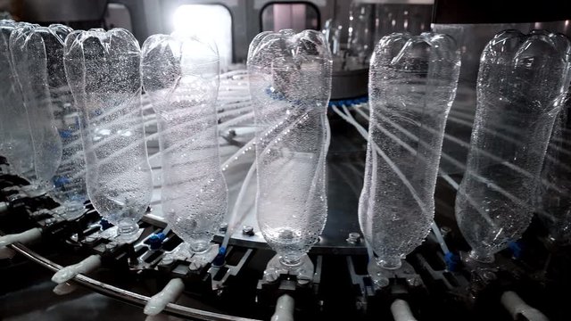 Production of plastic bottles rotating on bottling automatic conveyor line in plant. Ecological harm of plastic in world. Industrial manufacturing food plastic products in factory. Chemisrty industry.