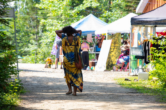 African woman viewed from the back wearing traditional clothes walking between trees and outdoor exhibitions Tents during a spiritual gathering