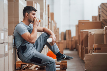 Storage worker sits and have a break. Eats sandwitch and drinks coffee