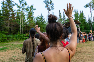 diverse people enjoy spiritual gathering, A close up of young caucasian woman with one arm raised in air during a shamanic ritual, viewed from the back