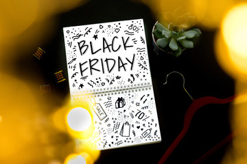 Black friday flat lay with note, succulent and shoulder on black background through garlands lights. Lettering Black friday and Doodle in note.