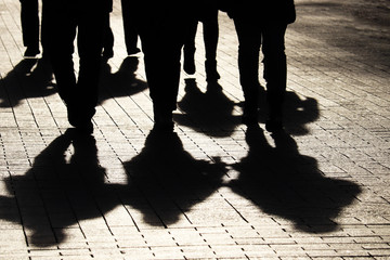 Silhouettes and shadows of people on the city street. Crowd walking down on sidewalk, concept of strangers, crime, society, gang or population - obrazy, fototapety, plakaty