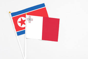 Malta and North Korea stick flags on white background. High quality fabric, miniature national flag. Peaceful global concept.White floor for copy space.