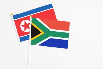 South Africa and North Korea stick flags on white background. High quality fabric, miniature national flag. Peaceful global concept.White floor for copy space.