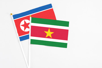 Suriname and North Korea stick flags on white background. High quality fabric, miniature national flag. Peaceful global concept.White floor for copy space.