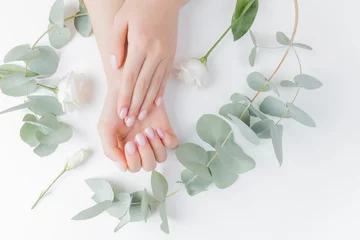Foto op Canvas Stijlvolle effen vrouwelijke hand manicure gel polish op witte bloem achtergrond eucalyptus, bovenaanzicht. Concept natuurlijke biologische huidverzorging © Parilov