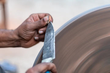 hands of construction worker sharpens a knife on sanding machine