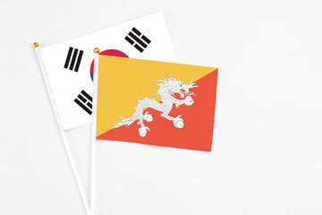 Bhutan and South Korea stick flags on white background. High quality fabric, miniature national flag. Peaceful global concept.White floor for copy space.