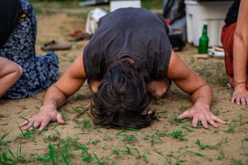 Diverse people enjoy spiritual gathering, close up on man in kneeling and bent forward facing pose,...