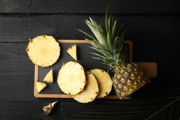 Cutting board with pineapple and palm branch on wooden background, top view