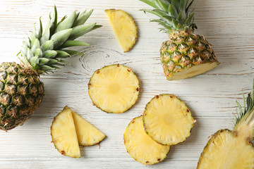 Pineapples and slices on white wooden background, top view