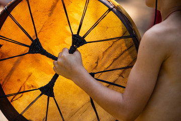 close up on shirtless little kid hands as he holding native sacred drum during a spiritual...