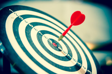 Red dart arrow hitting in the target center of dartboard on bullseye for Business focus concept.