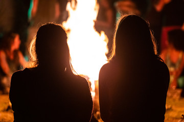 silhouette of two girls sitting in the front of the fire as they watching night musical show, seen...