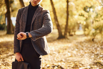 Close up view of young man in formal clothes that is in the autumn park at sunny day