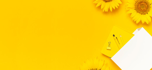 Top view flat lay of workspace desk styled design with sunflowers, white paper bag pencils pen...