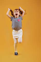 Cute little girl in casual clothes have fun in the studio against yellow background