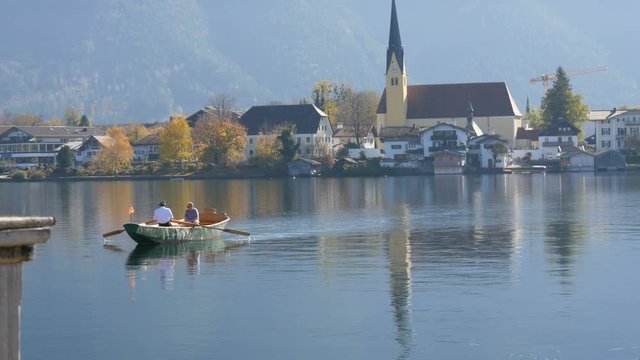 A boat ferryman ferries people to the other side, in the background of a beautiful, picturesque church on Lake Tegernsee, Bavaria, Germany