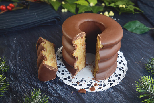 Cut open traditional German layered winter cake called 'Baumkuchen' glazed with chocolate, surrounded by seasonal decoration