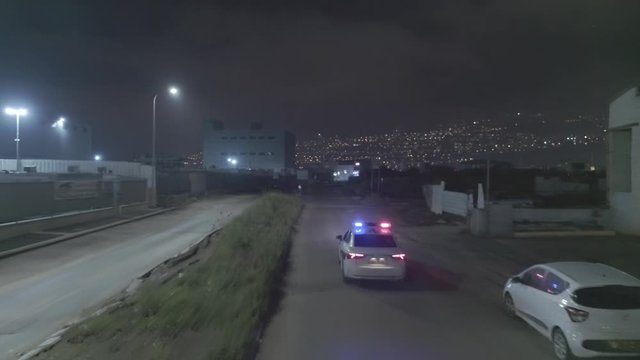 Night aerial footage of a police car driving down a dark urban area