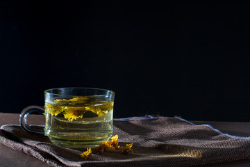 Cup of Chrysanthemum tea with dry flower on brown table cloth on black background. Healthy beverrage for drink. Herbs and medical concept.