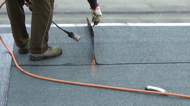 Worker preparing part of bitumen roofing felt roll for melting by gas heater torch flame. On the back of the sheath there is the stamp; Made in Italy; product