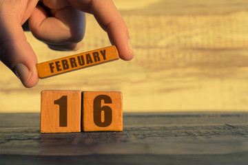 february 16th. Day 16 of month,calendar on a wooden cube. a woman's hand puts the name of the month on the number of the month on a wooden background winter, day of the year concept