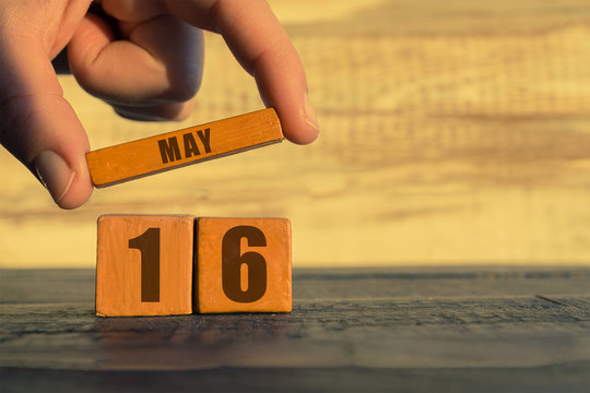 may 16th. Day 16 of month,calendar on a wooden cube. a woman's hand puts the name of the month on the number of the month on a wooden background spring, day of the year concept