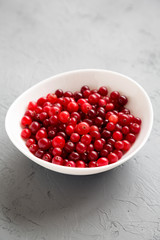Ripe organic cranberries in a white bowl over gray background, side view.