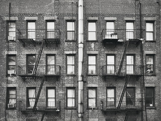 Black and white picture of an old brick house with fire escapes, New York, USA.