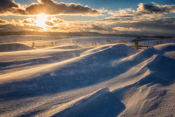 Snow storm, snowdrift and snow dust at sunset on the road, dramatic landscape of windy winter...